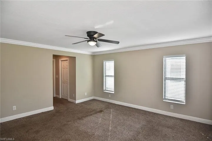 Spare room featuring dark colored carpet, plenty of natural light, and ornamental molding