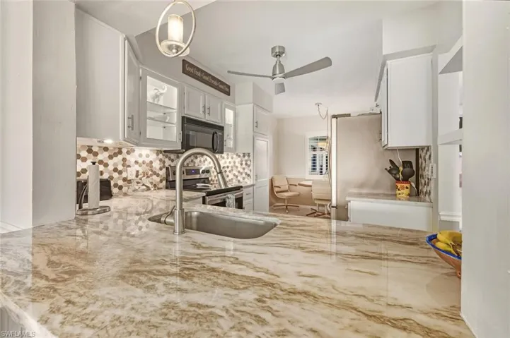 Kitchen with stainless steel appliances, white cabinetry, and light stone countertops