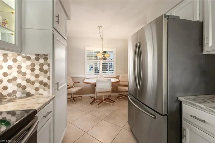 Kitchen with tasteful backsplash, decorative light fixtures, white cabinets, light tile patterned floors, and freestanding refrigerator