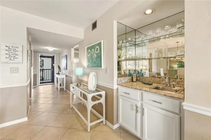 Indoor wet bar with white cabinets, light stone countertops, and light tile patterned flooring