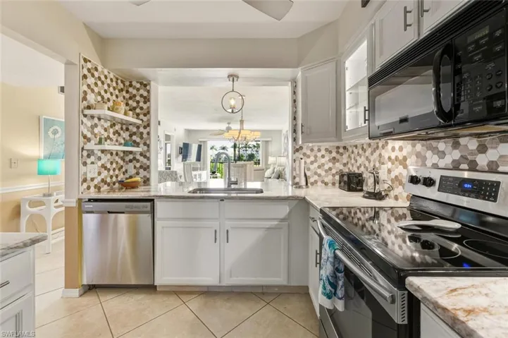 Kitchen with stainless steel appliances, white cabinetry, decorative light fixtures, and light stone countertops