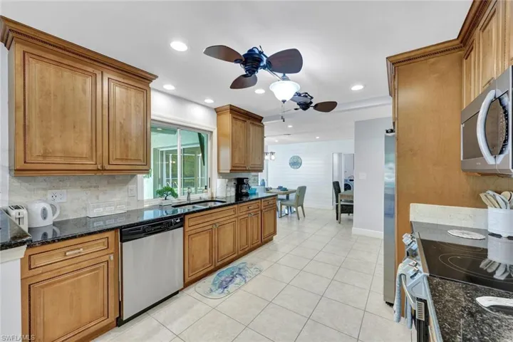 Kitchen featuring dark stone counters, brown cabinetry, a ceiling fan, stainless steel appliances, and recessed lighting