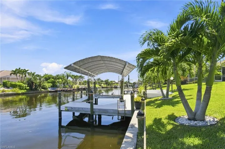 Waterfront property featuring a covered boat dock, direct canal access, manicured lawn, and mature palm trees