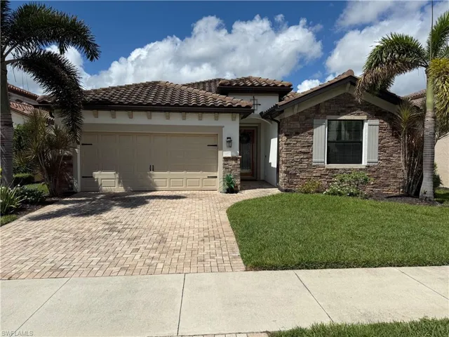 Mediterranean-inspired architecture featuring a tile roof, stone facade accents, paver driveway, and a manicured lawn