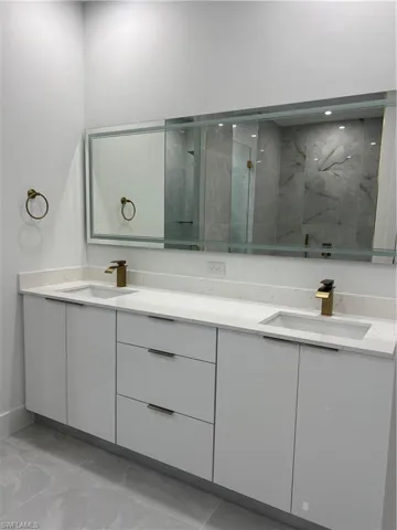 Bathroom featuring double vanity, a marble finish shower, and marble finish flooring