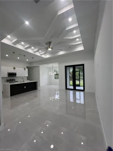 Unfurnished living room featuring a chandelier, ceiling fan, light marble finish flooring, recessed lighting, and coffered ceiling