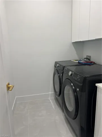Laundry room with washing machine and dryer, cabinet space, and light marble finish flooring