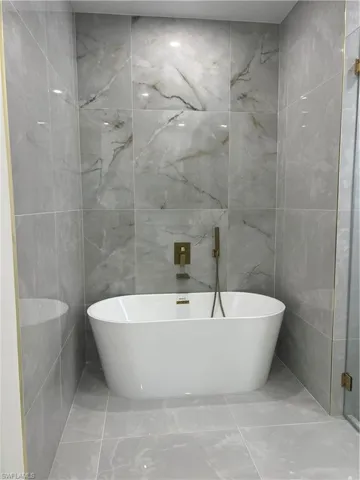 Full bathroom featuring tile walls, marble finish flooring, and a freestanding tub