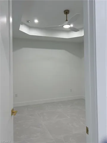 Unfurnished room with a tray ceiling, marble look tile flooring, and ceiling fan