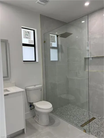 Bathroom featuring vanity, marble look tile flooring, walk in shower, and recessed lighting