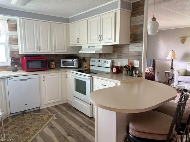 Kitchen featuring white appliances, wood-type flooring, decorative light fixtures, and white cabinets