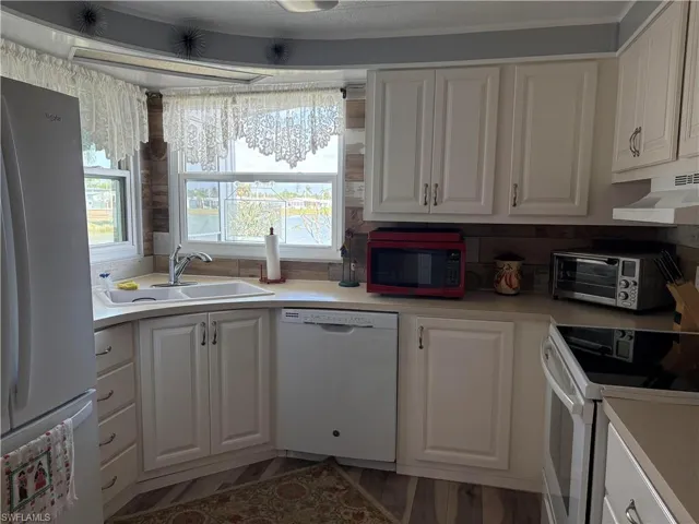 Kitchen with sink, dark wood-type flooring, white cabinets, and white appliances