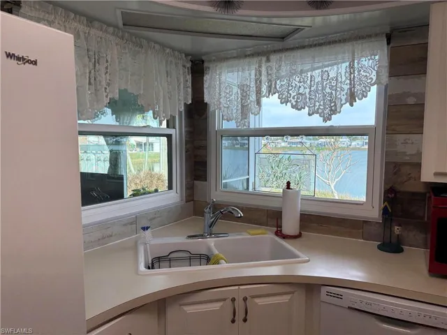 Kitchen featuring plenty of natural light, white dishwasher, sink, and white cabinets