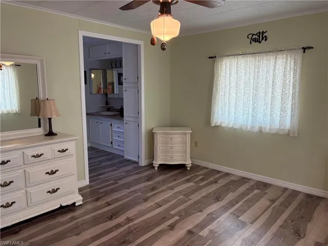 Unfurnished bedroom with sink, ensuite bath, dark wood-type flooring, and ornamental molding