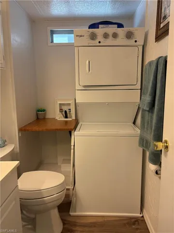 Bathroom featuring vanity, stacked washer / drying machine, hardwood / wood-style floors, and toilet