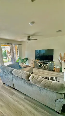 Spacious living area featuring light-toned wood-finish flooring, a ceiling fan, and sliding glass doors providing access to the exterior