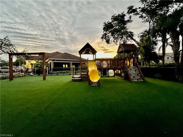 Expansive recreation area featuring a multi-level play structure with a yellow enclosed slide, rock climbing wall, and swing set