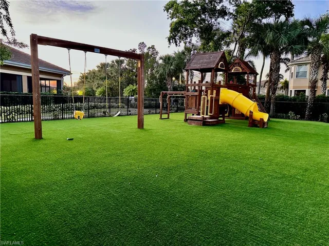 Recreational area featuring a wooden playset with a yellow slide, a swing set, and artificial turf surfacing
