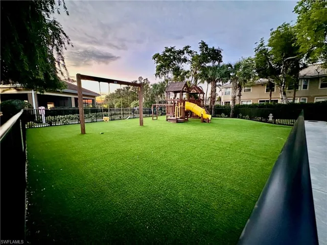 Landscaped recreation area featuring a swing set and play structure with a yellow slide, all set on artificial turf