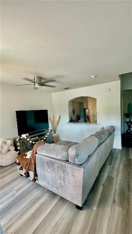 Living area featuring wood-finish flooring, a ceiling fan, and a pass-through window with an arched opening to the kitchen