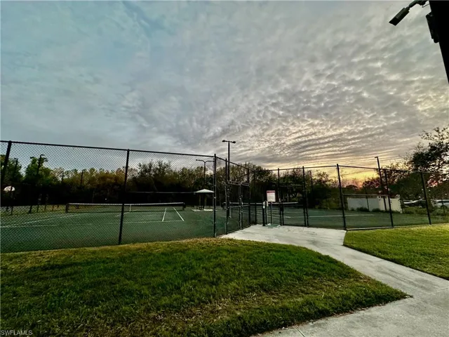 Tennis court featuring green hardcourt surfacing, perimeter fencing, and overhead lighting fixtures