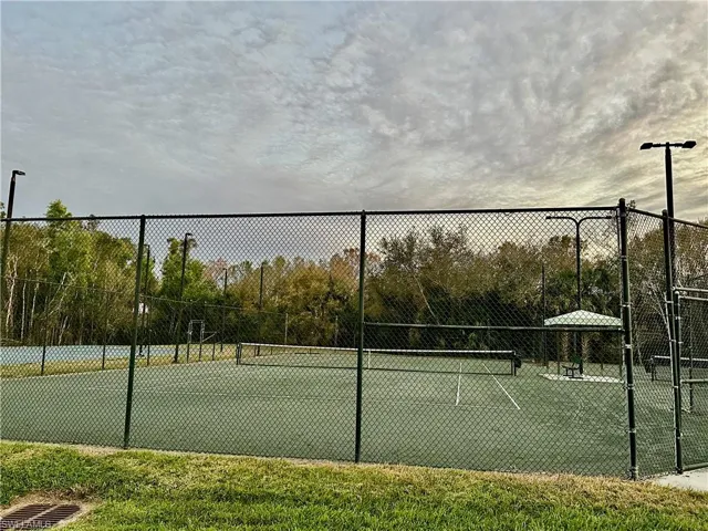 Tennis court featuring a green playing surface, perimeter fencing, and overhead lighting