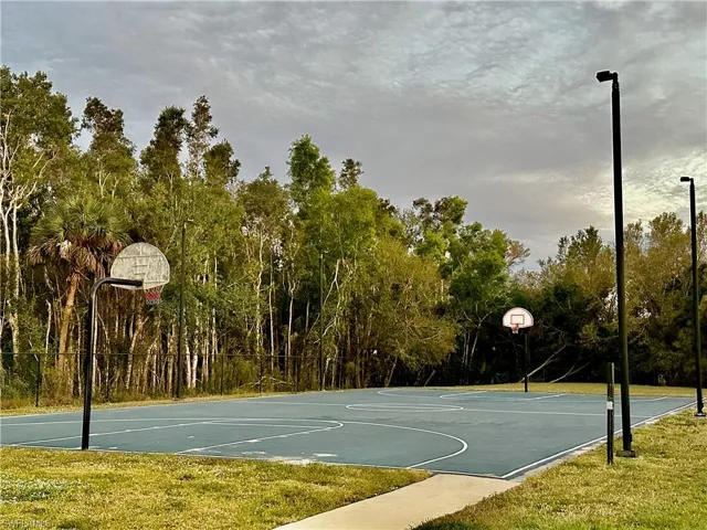Outdoor basketball court featuring a blue playing surface with white line markings, two basketball hoops, and perimeter lighting