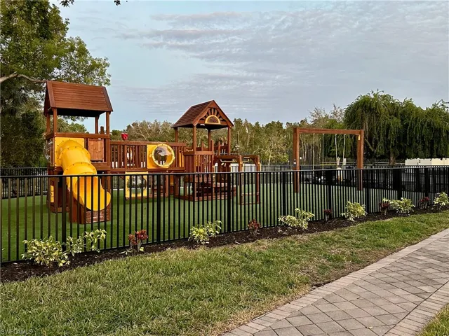 Playground area featuring a multi-level wooden structure with a yellow slide, a swing set, and a tunnel component