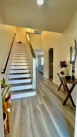Two-story entry featuring light wood-finish flooring, a white staircase with a contrasting dark handrail, and an arched doorway