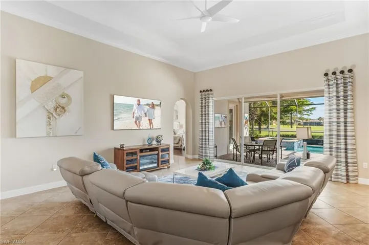 Living area with a raised ceiling, arched walkways, light tile patterned floors, crown molding, and a ceiling fan