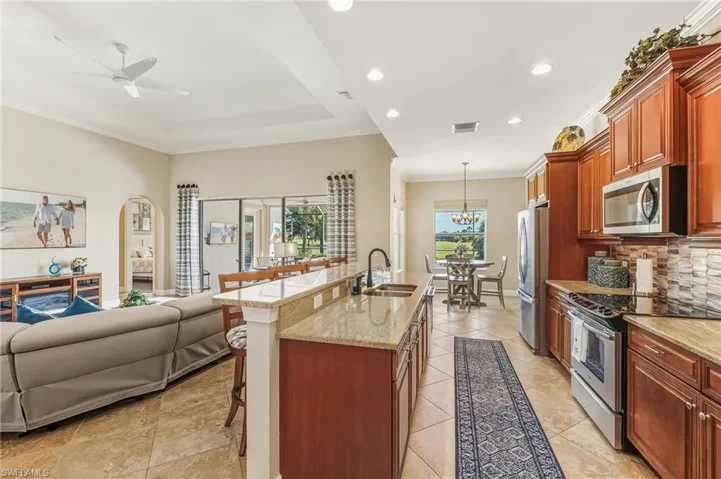 Kitchen with open floor plan, a kitchen bar, appliances with stainless steel finishes, ornamental molding, and light stone countertops