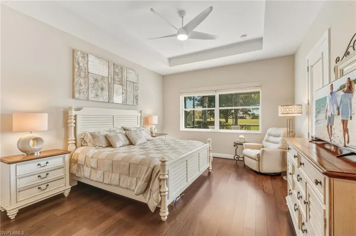 Bedroom with dark wood-type flooring, a raised ceiling, and a ceiling fan