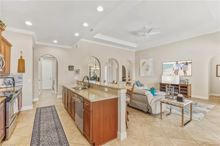 Kitchen featuring arched walkways, light stone countertops, brown cabinetry, appliances with stainless steel finishes, and ornamental molding