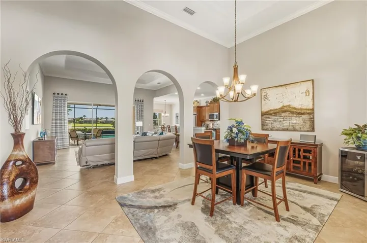 Dining space with arched walkways, crown molding, beverage cooler, a towering ceiling, and light tile patterned floors
