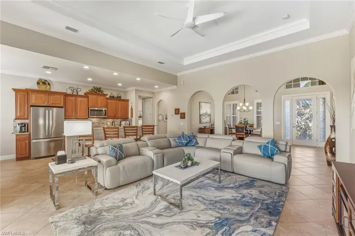 Living area with a chandelier, arched walkways, a raised ceiling, crown molding, and light tile patterned floors