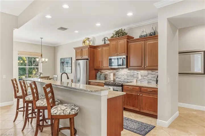 Kitchen featuring brown cabinets, ornamental molding, a breakfast bar, light tile patterned floors, and light stone counters