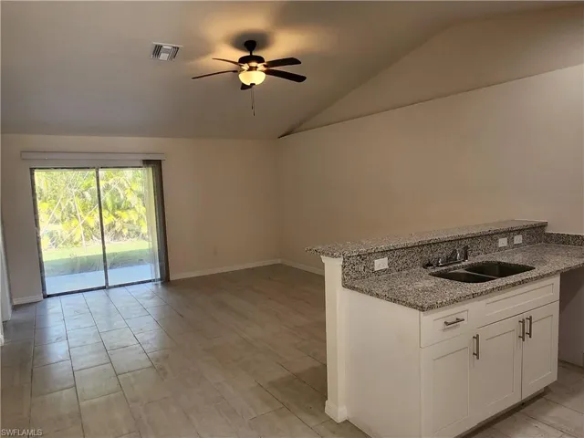 Kitchen featuring ceiling fan, vaulted ceiling, sink, white cabinets, and light stone counters