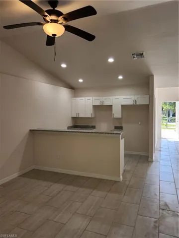 Kitchen featuring vaulted ceiling, ceiling fan, white cabinetry, and light stone countertops