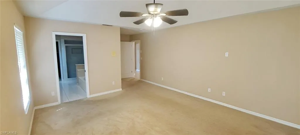 Unfurnished bedroom featuring light colored carpet, ceiling fan, and ensuite bath