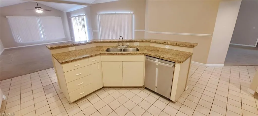 Kitchen featuring stainless steel dishwasher, light carpet, sink, and vaulted ceiling