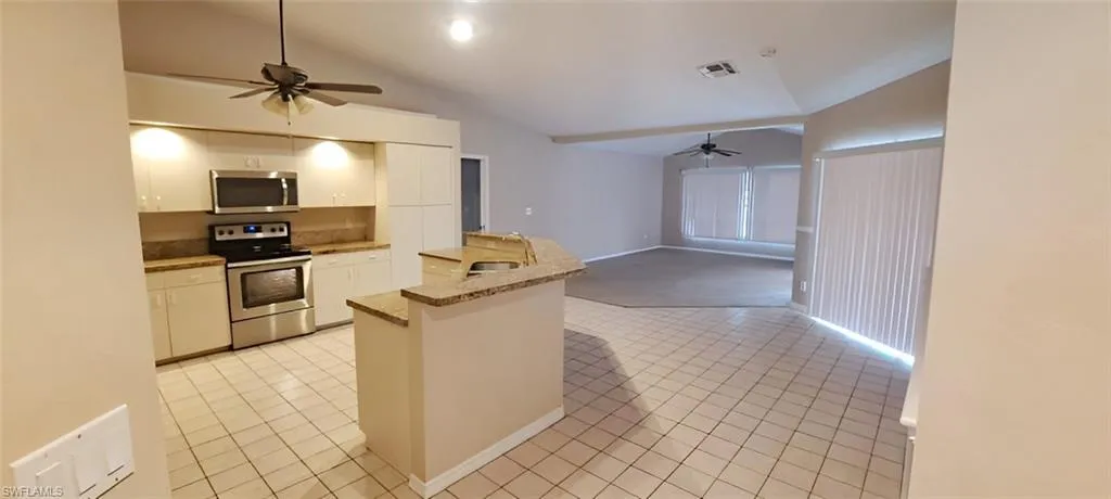 Kitchen with stainless steel appliances, vaulted ceiling, kitchen peninsula, light tile patterned floors, and white cabinetry