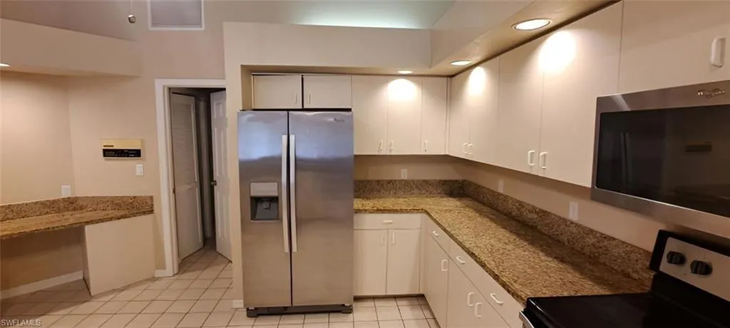 Kitchen with stone counters, appliances with stainless steel finishes, and white cabinets