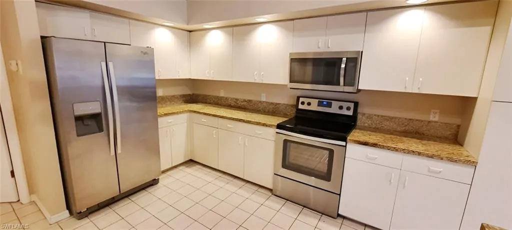 Kitchen featuring white cabinets, stainless steel appliances, light tile patterned floors, and light stone countertops