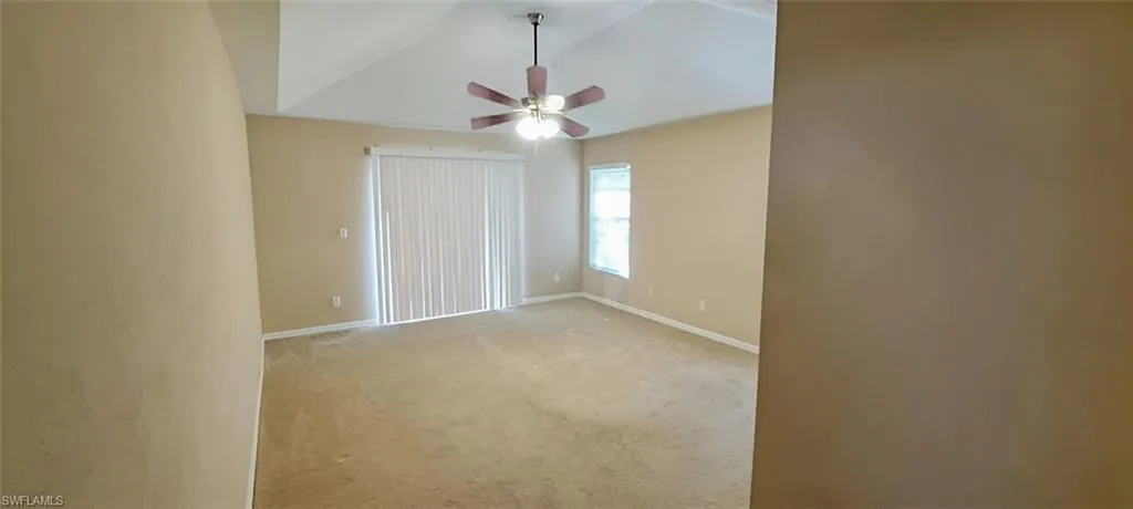 Carpeted empty room featuring lofted ceiling and ceiling fan