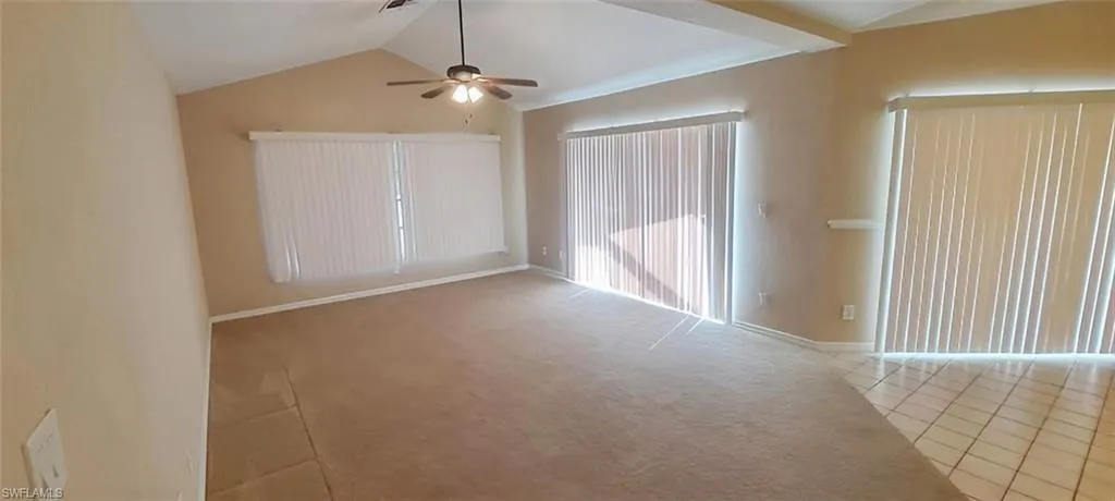Empty room with lofted ceiling, light carpet, and ceiling fan