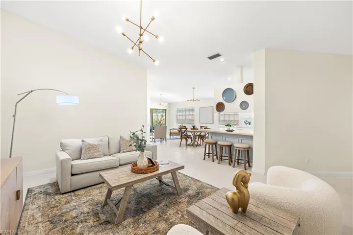 Living room with lofted ceiling, an inviting chandelier, light tile patterned floors, baseboards, and visible vents