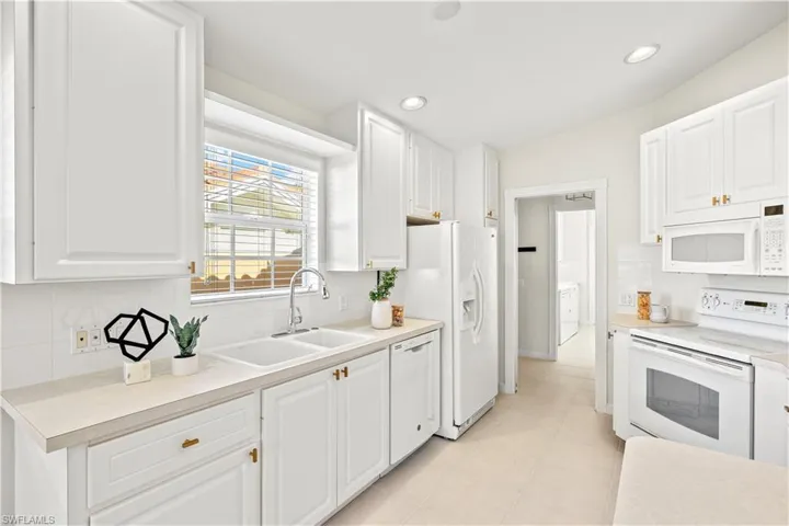 Kitchen with white cabinets, a sink, backsplash, and white appliances