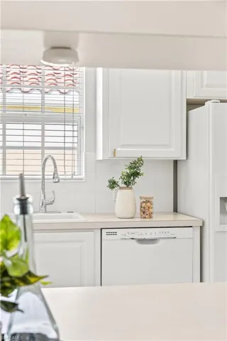 Kitchen featuring light countertops, white appliances, tasteful backsplash, white cabinetry, and a sink