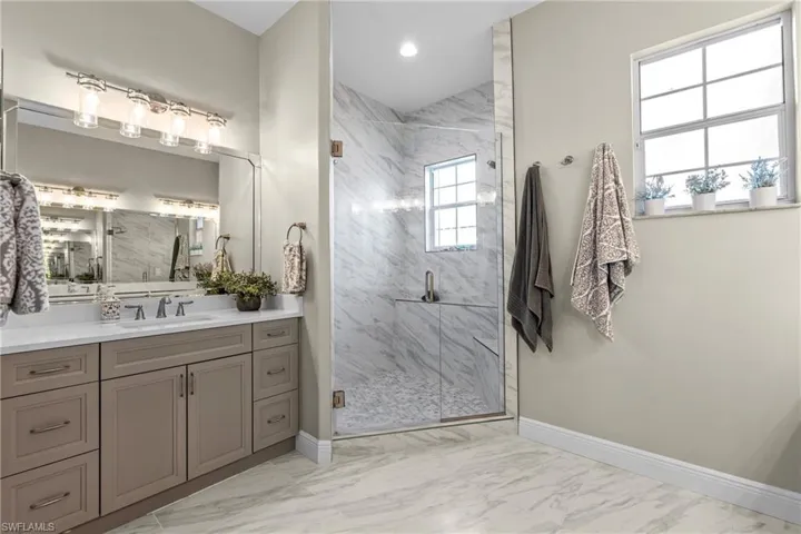 Spacious bathroom featuring a large vanity with ample storage, dual sinks, a contemporary glass-enclosed shower, and elegant tile flooring