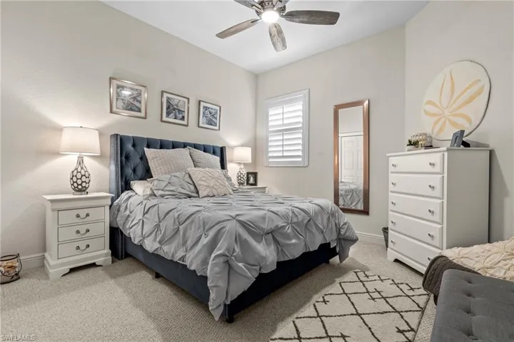 Plush carpet flooring, a ceiling fan with integrated lighting, and white plantation shutters on the window